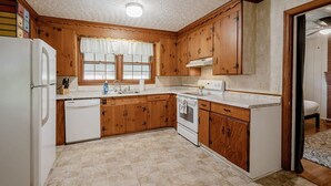 A compact kitchen with wooden cabinets, a white refrigerator, a dishwasher, and a stove.
