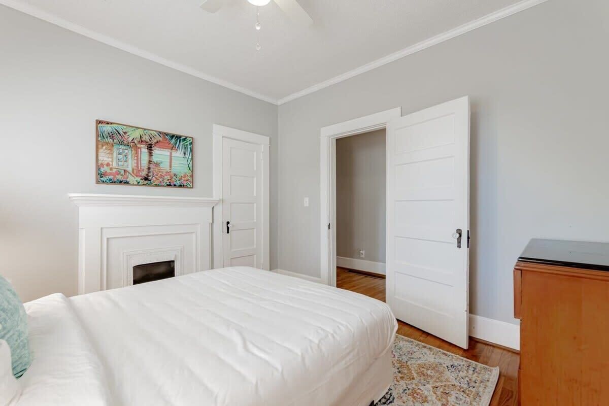 A bedroom with a bed, a fireplace, a door, and a painting on the wall.