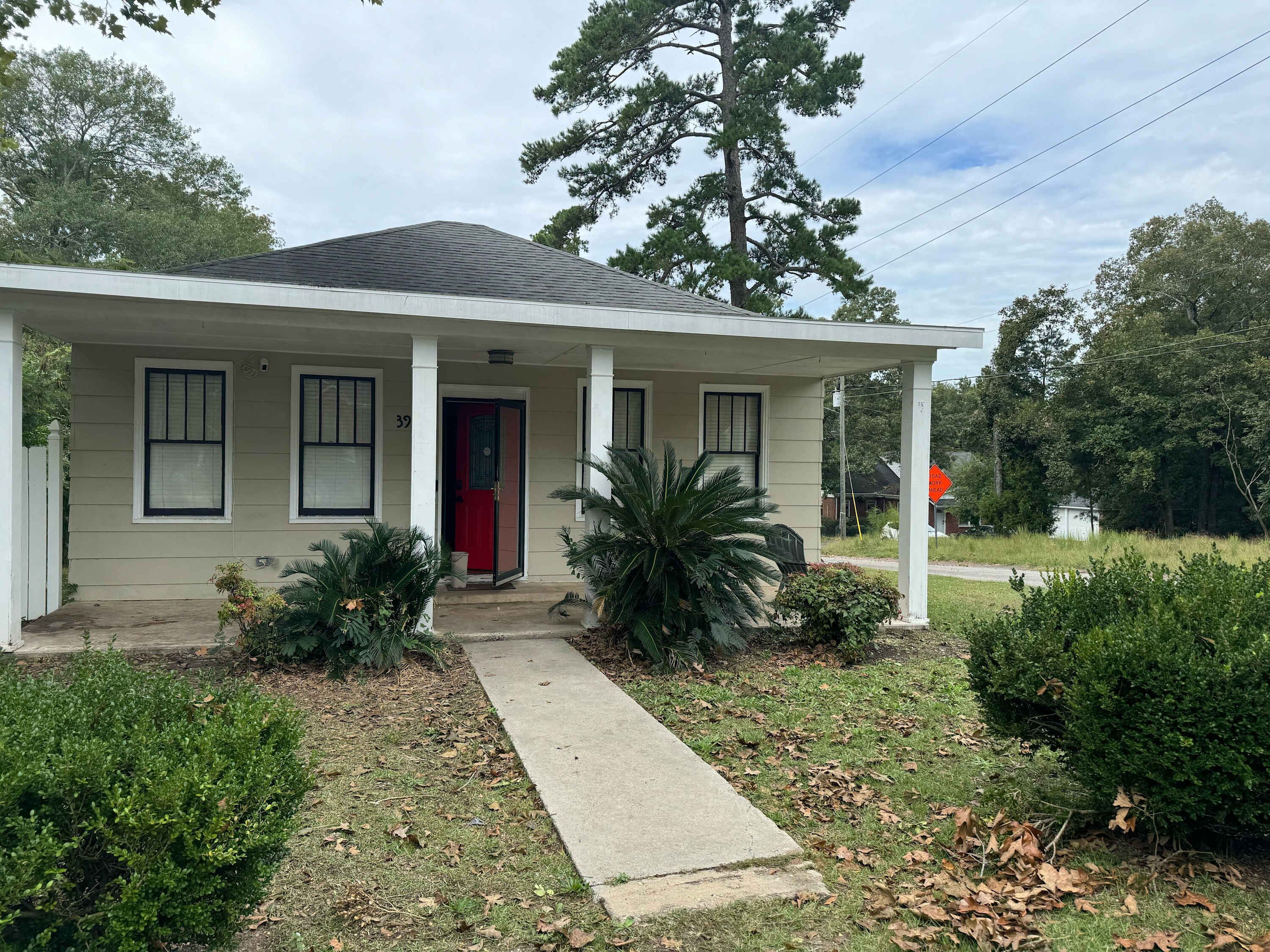 A single-story house with a red door, white siding, and a covered porch.