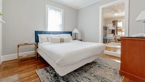 A bedroom with a bed, a nightstand, a lamp, a ceiling fan, and a view of a hallway.