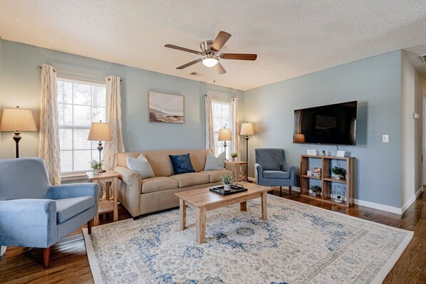 Relax in this inviting living space with a sofa, chair, and coffee table, perfect for unwinding with a flat-screen TV and ceiling fan.