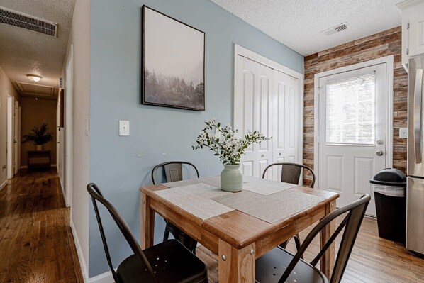 Enjoy meals in this dining area with a table for four, a vase with flowers, and a framed picture above.