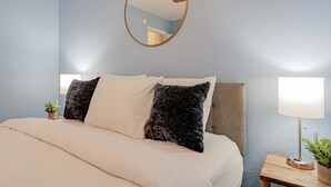 A bedroom with a bed, pillows, a bedside table with a lamp, and a mirror on the wall. - Close to USC & Midtown-Downtown - Newly Renovated! (Columbia)