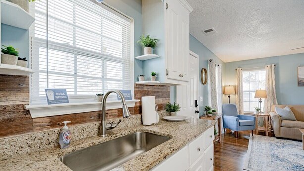 A modern kitchen with granite countertops, a stainless steel sink, and white cabinetry. There is a window with blinds, a sink with a soap dispenser, and a trash can labeled "Recycling." - Close to USC & Midtown-Downtown - Newly Renovated! (Columbia)