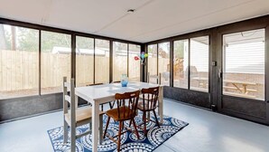 Un patio cubierto con mesa y sillas, ventanas amplias y vista a una cerca de madera.