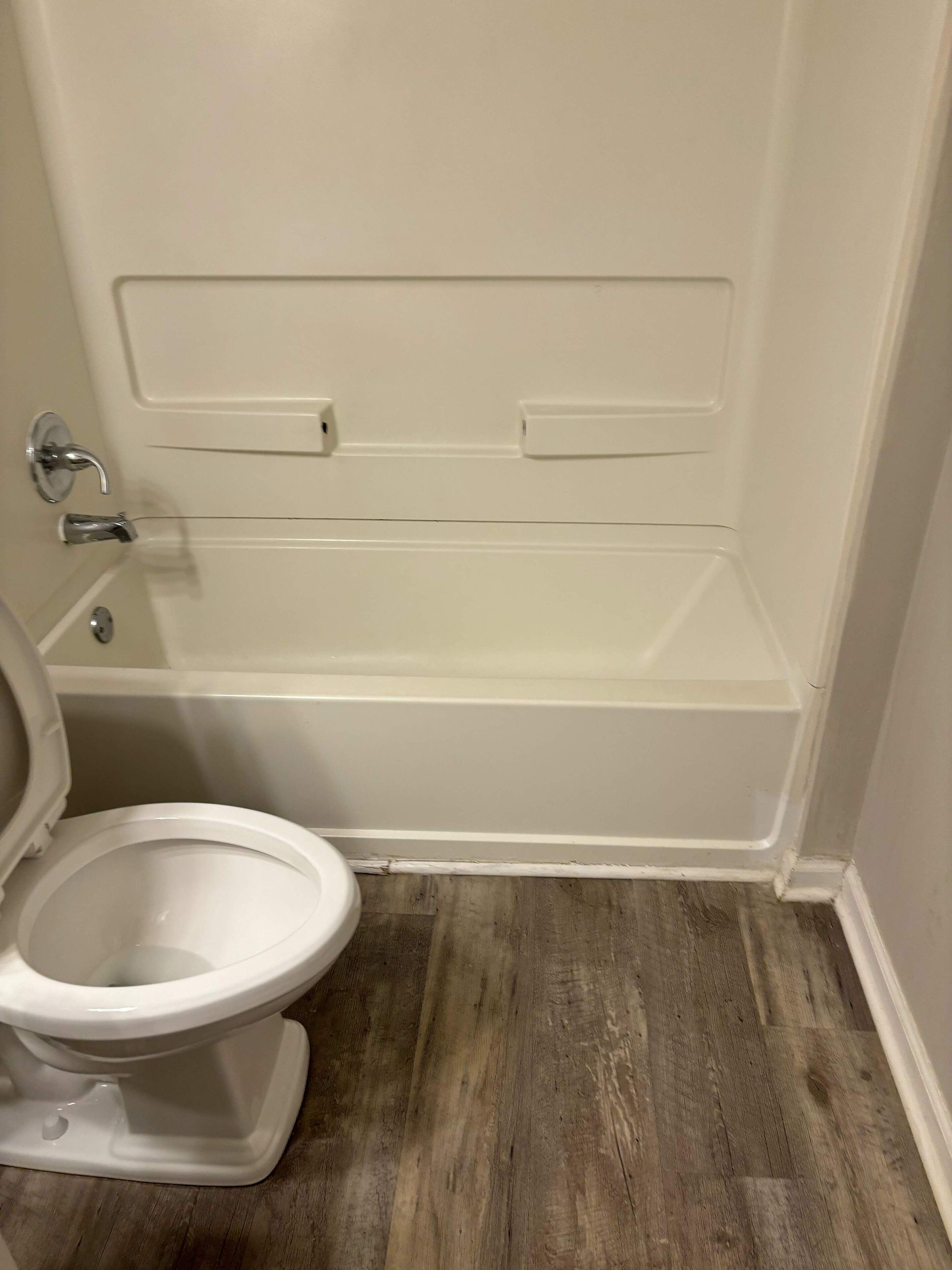 Ein Badezimmer mit einer weißen Badewanne, einer Toilette und Holzboden.