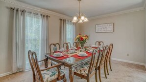 Comedor con mesa de vidrio, individuales rojos y sillas con estampado floral.