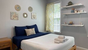 Un dormitorio con cama, mesita de noche, decoración en la pared y una ventana con cortinas.