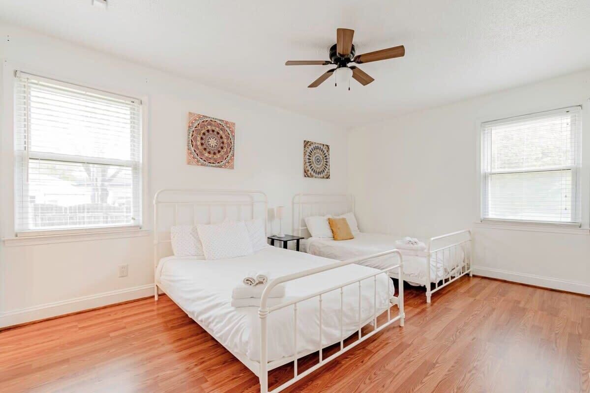 A bedroom with two beds, a ceiling fan, and two windows with blinds.