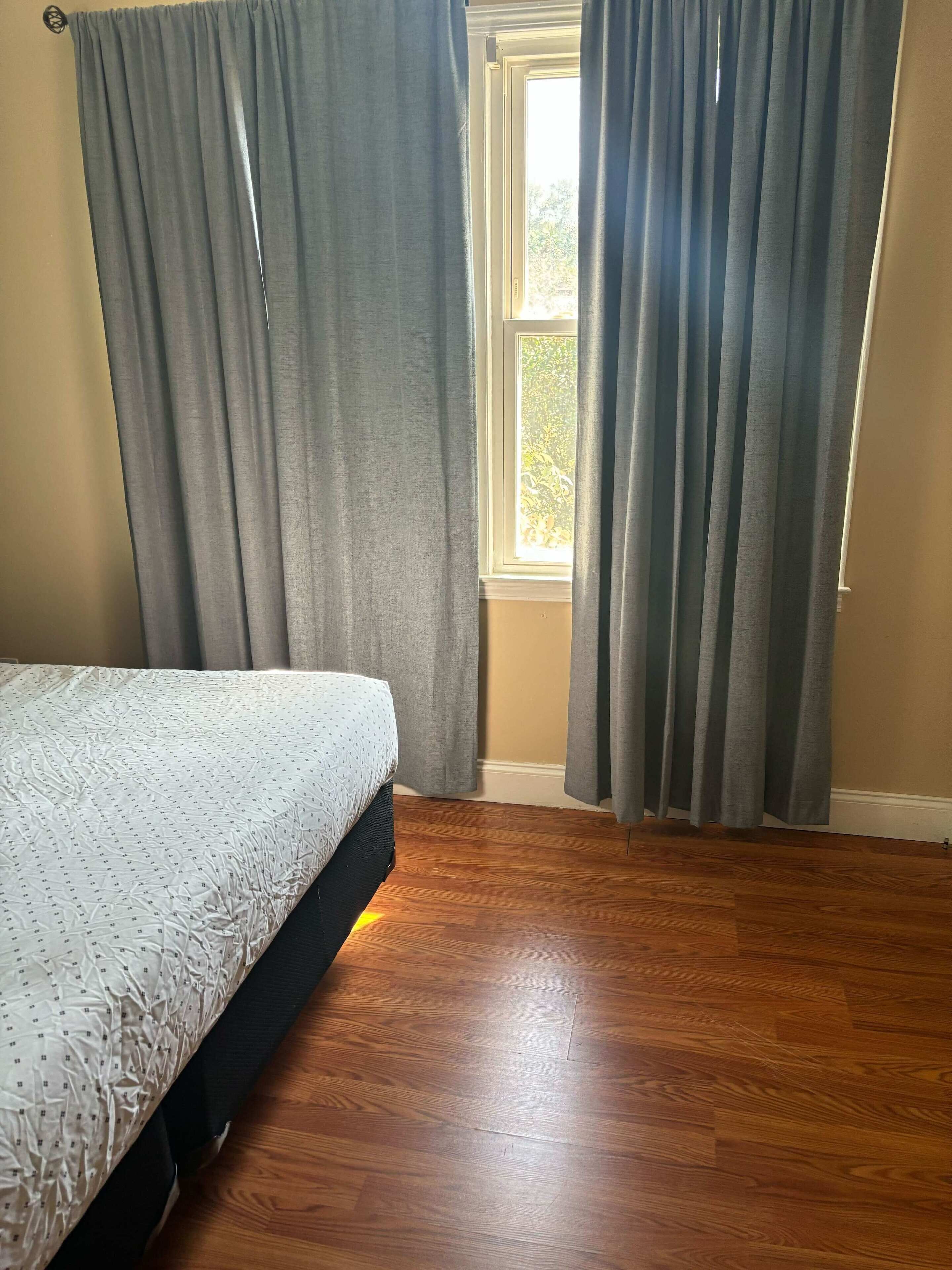 Ein Schlafzimmer mit einem Bett, Holzboden und grauen Vorhängen.