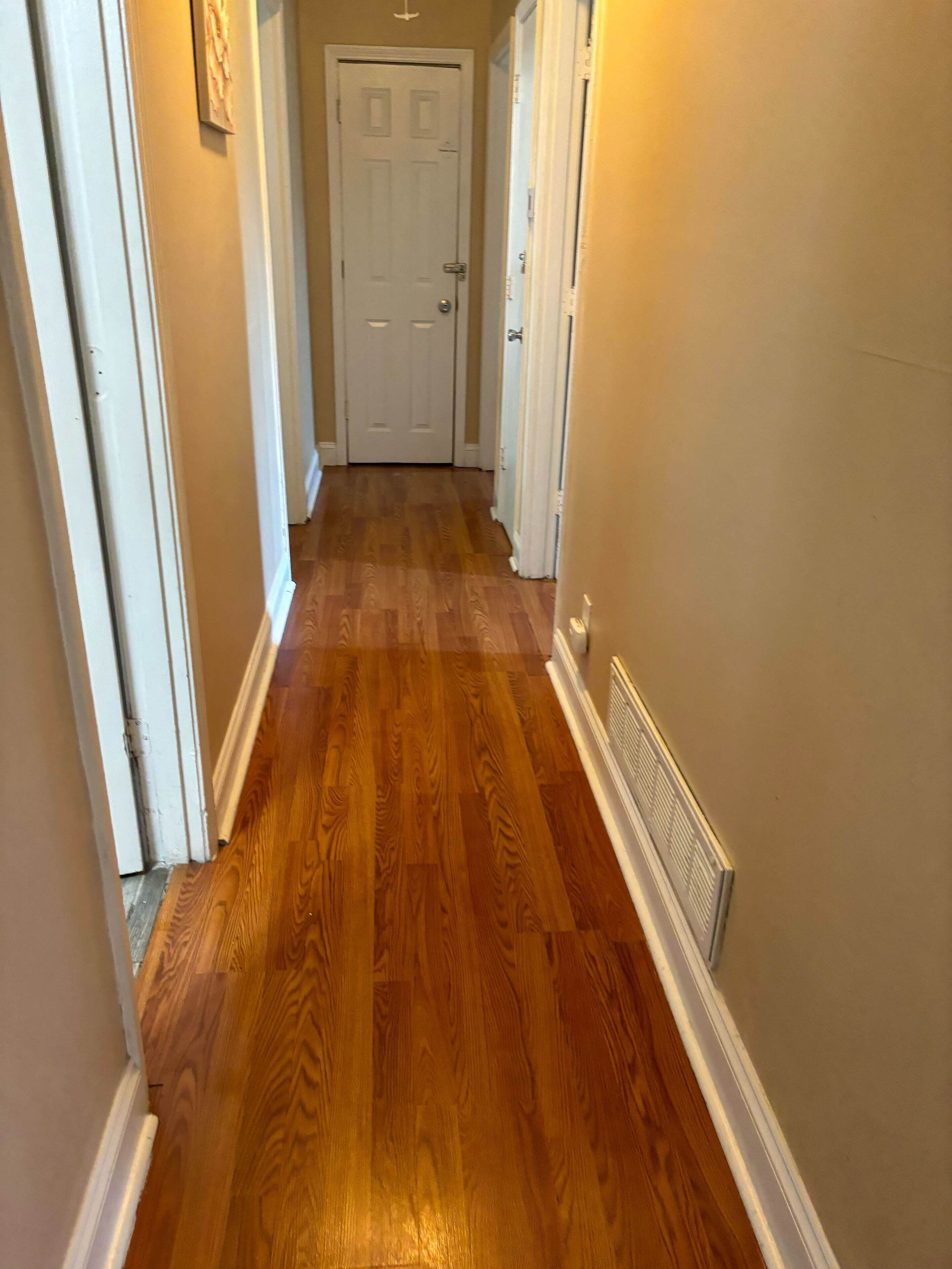 Un couloir doté d’un plancher en bois, de boiseries blanches et d’une porte au fond.