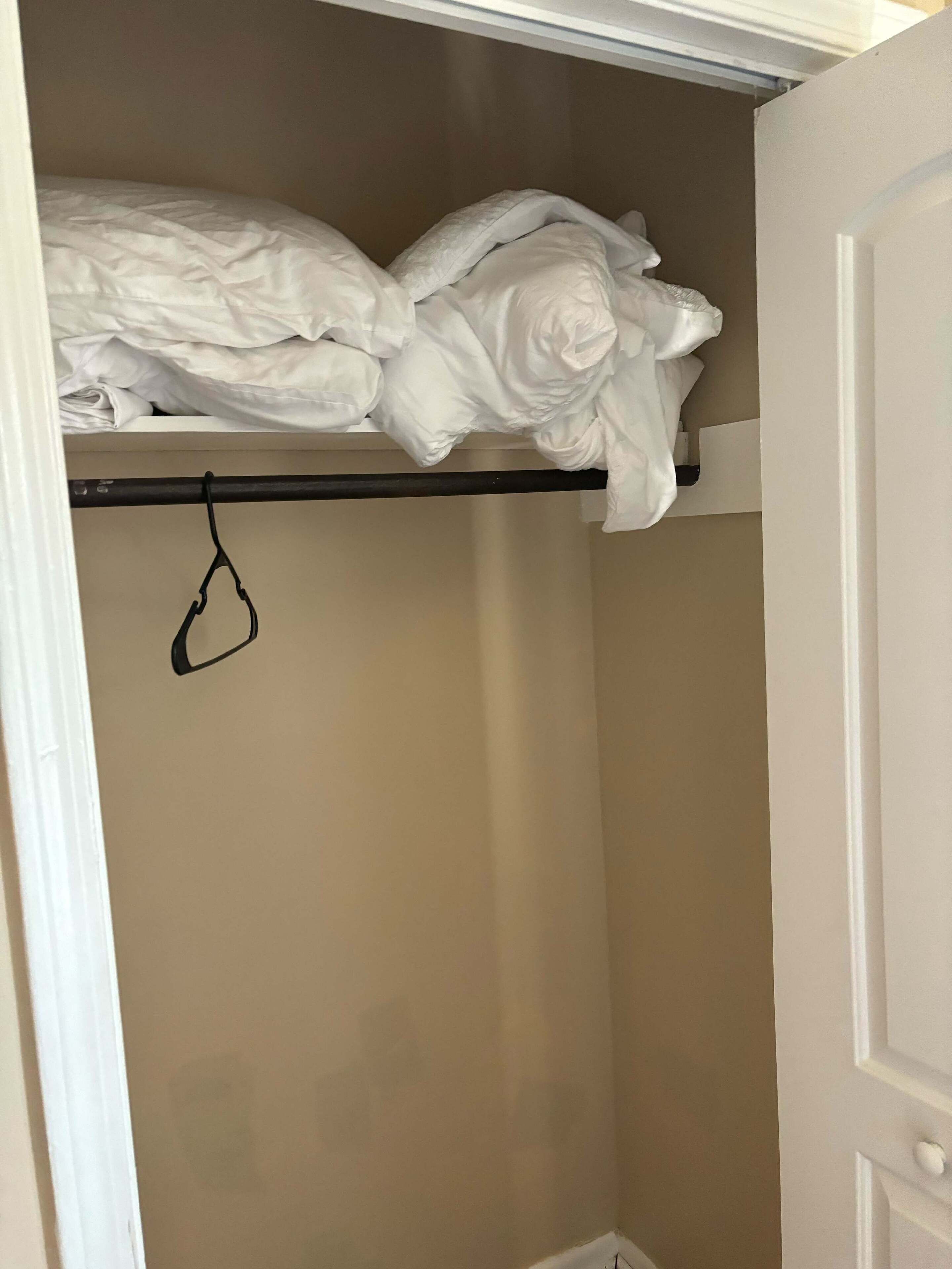 A closet with a hanging rod and a folded bed at the top.