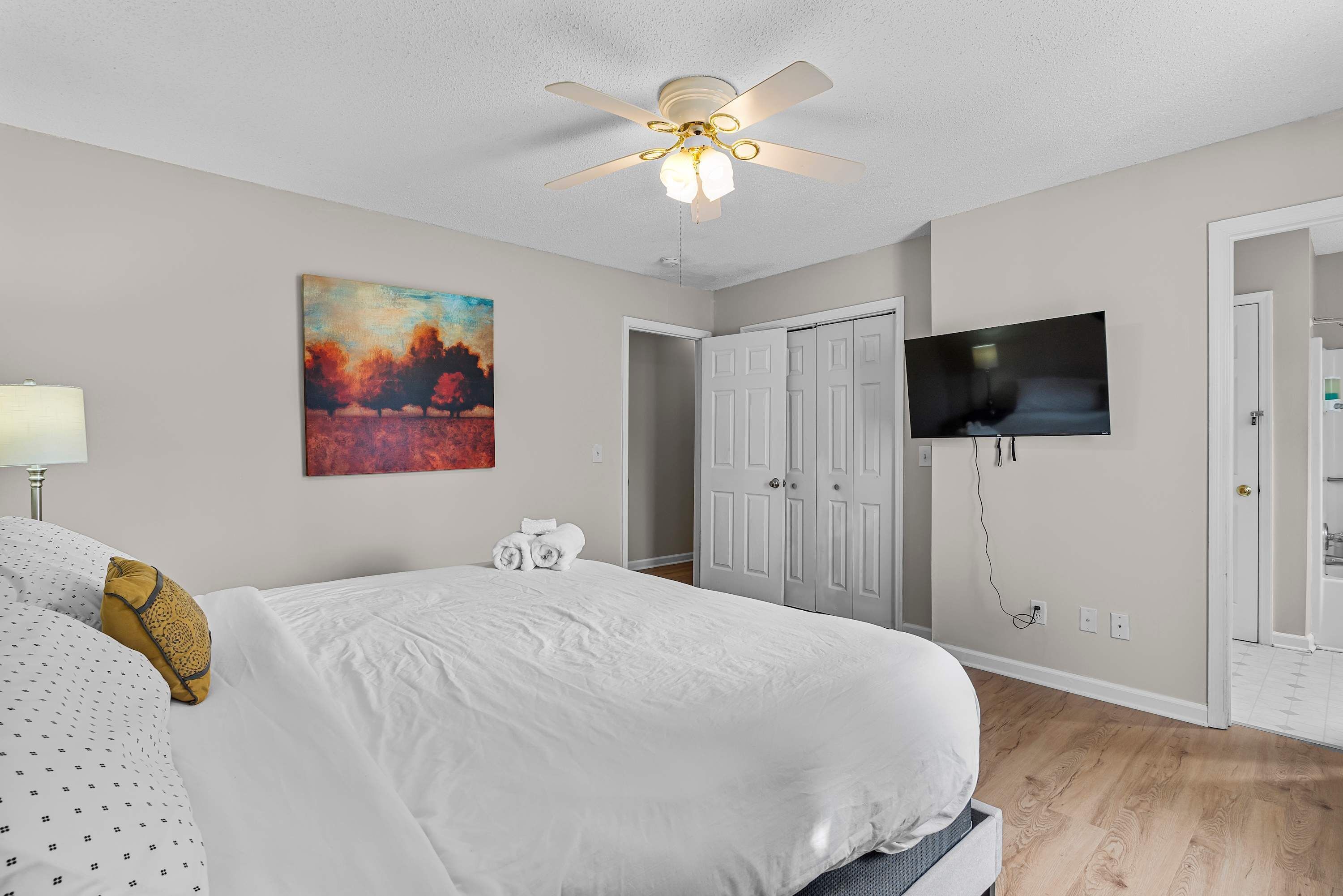Une chambre à coucher avec un lit, un ventilateur de plafond, un tableau, une armoire et un téléviseur.