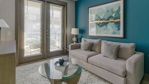 A living room with a beige sofa, a glass coffee table, and a painting on the wall. - Landing | Modern 1BD, Gym (Houston)