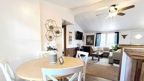 A dining area with a round table and chairs, a living room with a sofa and a TV, and a ceiling fan. - Mins to Downtown & Working Desk - Gamecock Roost (West Columbia)