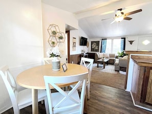 A dining area with a round table and chairs, a living room with a sofa and a TV, and a ceiling fan.
