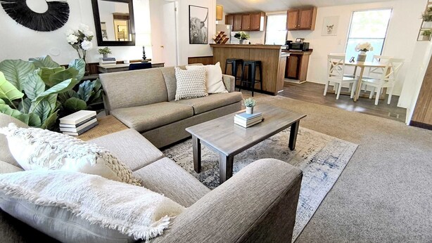 A living room with a sofa, coffee table, and a kitchen in the background. - Mins to Downtown & Working Desk - Gamecock Roost (West Columbia)