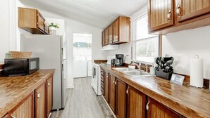 A modern kitchen with wooden cabinets, a refrigerator, a microwave, a coffee maker, and a sink. - Mins to Downtown & Working Desk - Gamecock Roost (West Columbia)
