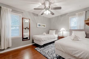 A bedroom with a ceiling fan, two beds, a nightstand with a lamp, a mirror, and a window with curtains.