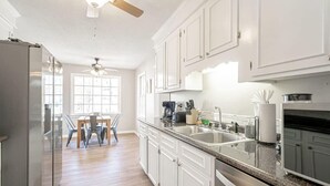 Une cuisine moderne avec des meubles blancs, un plan de travail en granit et un coin repas comprenant une table et des chaises.
