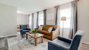 A modern living room with a brown sofa, two armchairs, a wooden coffee table, and a patterned rug.