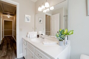 Une salle de bain avec un meuble-lavabo blanc, un grand miroir et une plante en pot.