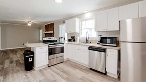 A modern kitchen with white cabinets, stainless steel appliances, and a wooden floor.