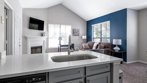 A modern kitchen with a built-in dishwasher, a fireplace, and a dining area with a couch and a lamp.