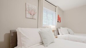 Une chambre d’hôtel avec deux lits, une fenêtre avec des stores, une lampe et un tableau au mur.