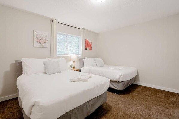 A hotel room with two beds, a window, and a nightstand with a lamp.