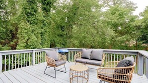 Une terrasse dotée de meubles en osier, notamment des chaises et un canapé, entourée d’une végétation luxuriante.