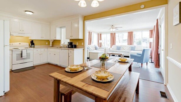 Een moderne keuken met witte kasten, een houten eettafel met servies, en een plafondventilator.