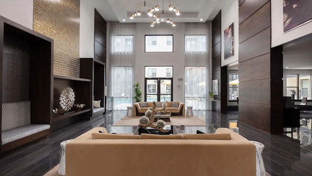 A spacious lobby with a central seating area, large windows, and a modern chandelier. - Landing | Amazing 2BD, Gym (Houston)