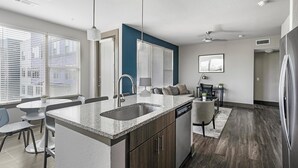 A modern kitchen with granite countertops, a built-in sink, and a dining area with a table and chairs. - Landing | Amazing 2BD, Gym (Houston)