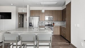 A modern kitchen with a large island, stainless steel appliances, and wooden cabinets. - Landing | Amazing 2BD, Gym (Houston)