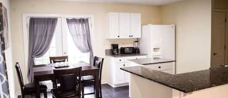 A compact kitchen with white cabinets, a black countertop, and a refrigerator.