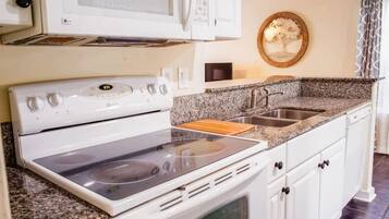A kitchen with a white stove, granite countertop, and a microwave above it.