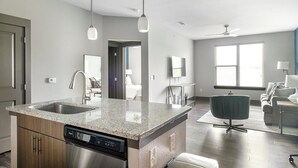 A modern kitchen with granite countertops, a dishwasher, and a dining area with a round table and chairs. - Landing | Spectacular 1BD, Gym (Houston)
