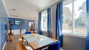 A dining area with a wooden table and blue chairs, a mirror on the wall, and a view of the outdoors through large windows. - Near Downtown & On the Water! Sweet Retreat! (Columbia)