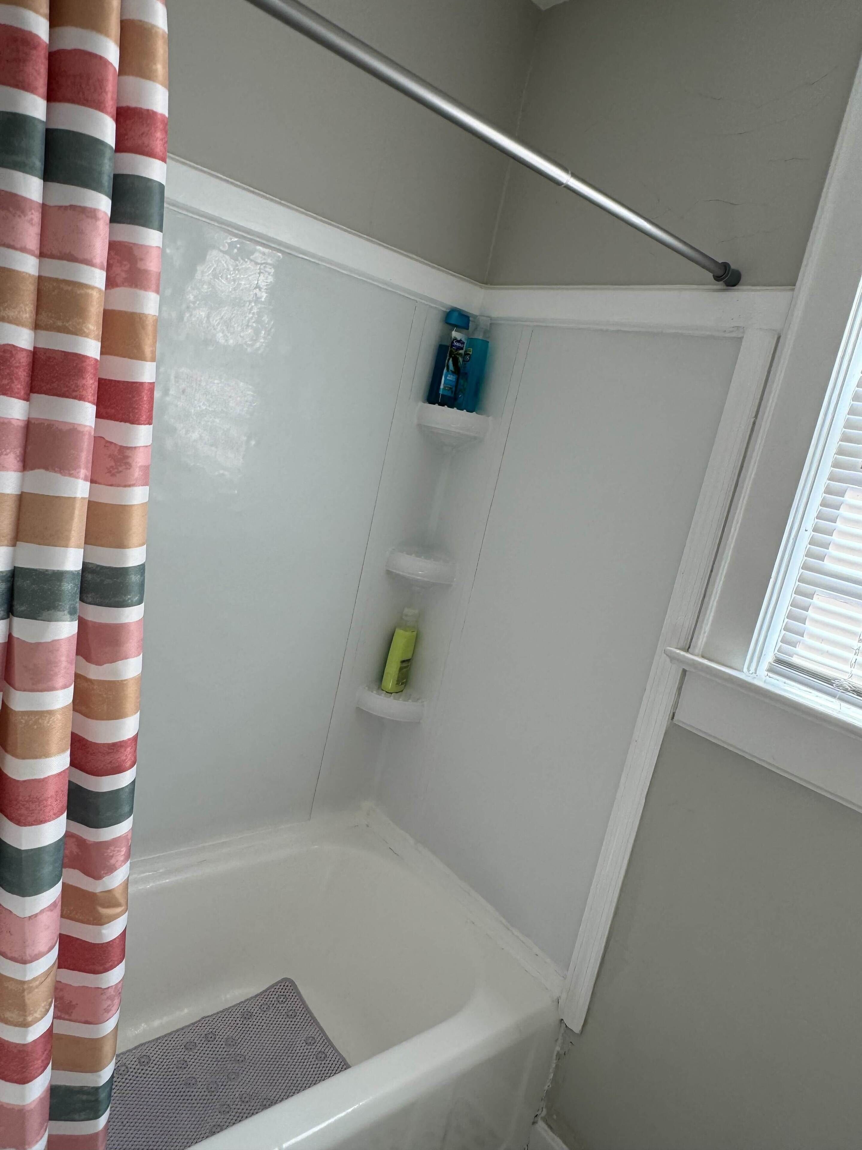 A bathroom with a white bathtub, striped curtains, and a shower area with shelves holding toiletries.
