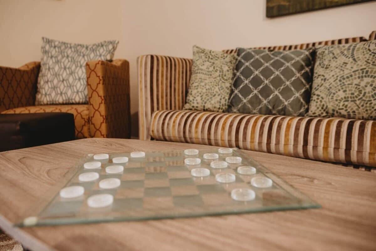 A checkered board game on a wooden table with striped sofas and patterned cushions in the background.