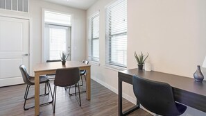 A room with a wooden dining table, four chairs, a potted plant, and a vase on a side table.