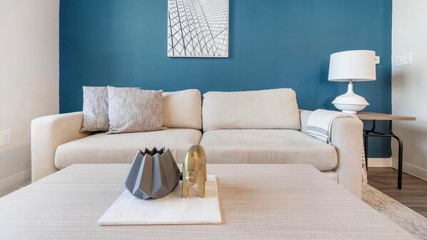 A living room with a blue wall, a white sofa, a coffee table with decorative items, and a lamp on a side table.