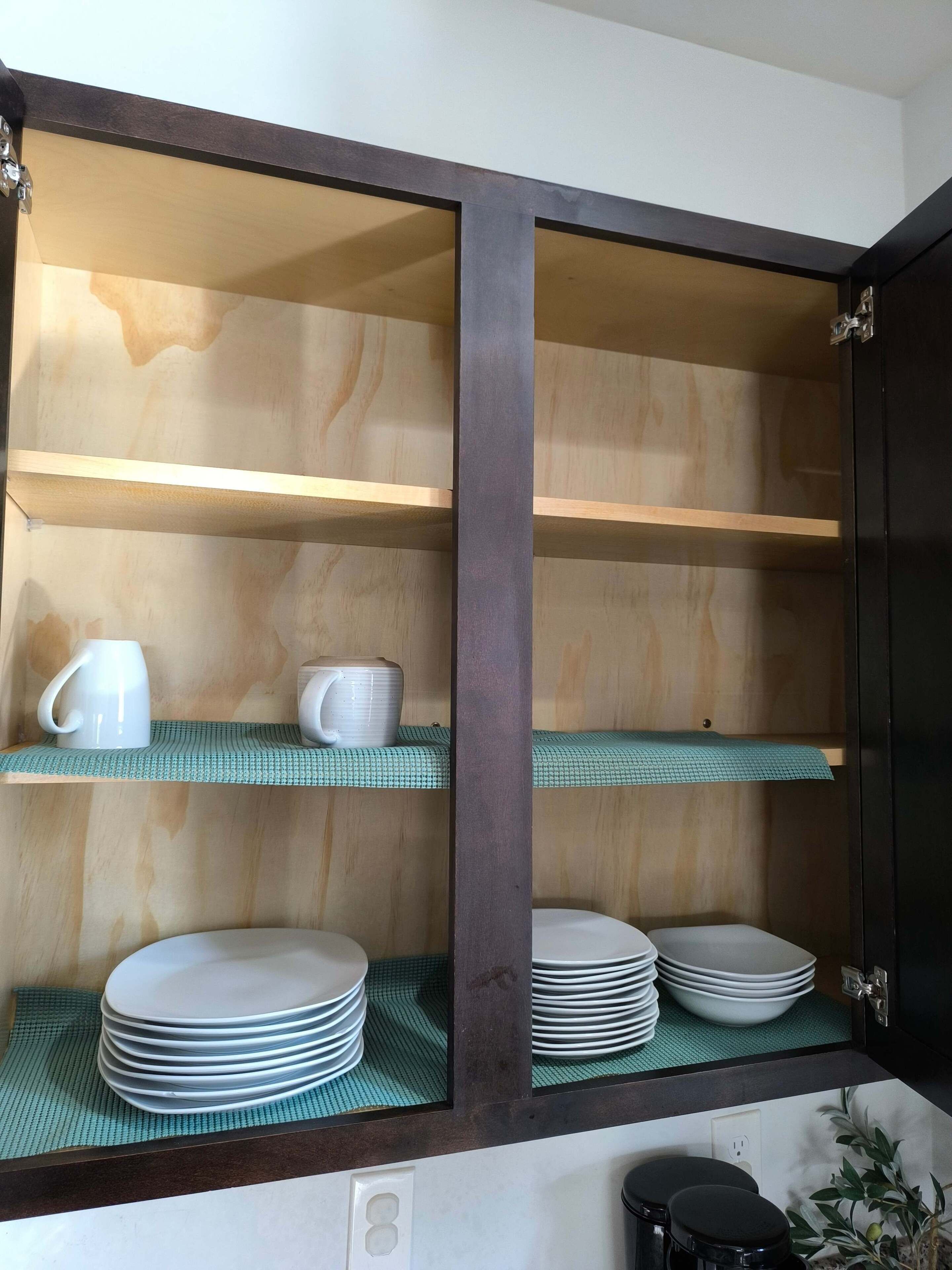 Una cucina con mobili in legno, mensole verdi e piatti e tazze bianche.
