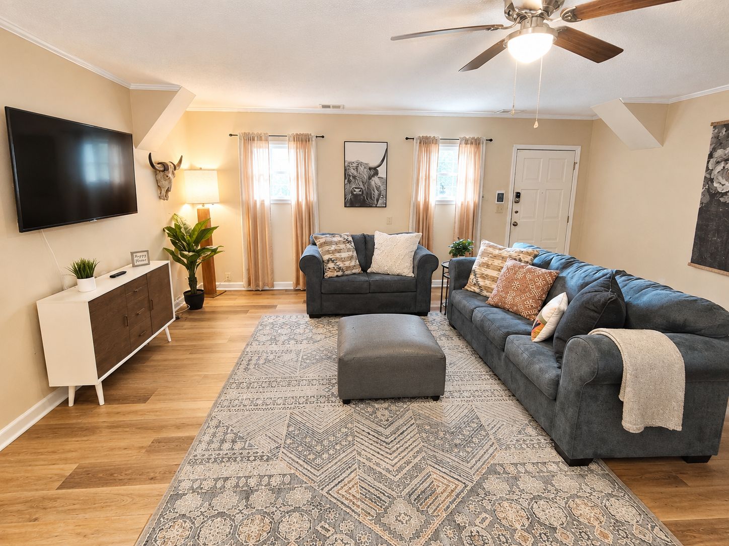 A living room with a sofa, ottoman, TV, and a ceiling fan.