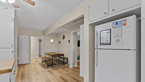 A kitchen with a wooden floor, white cabinets, a refrigerator, and a dining area with a table and chairs. - USC & Downtown Gem: Modern Family Home! (Columbia)