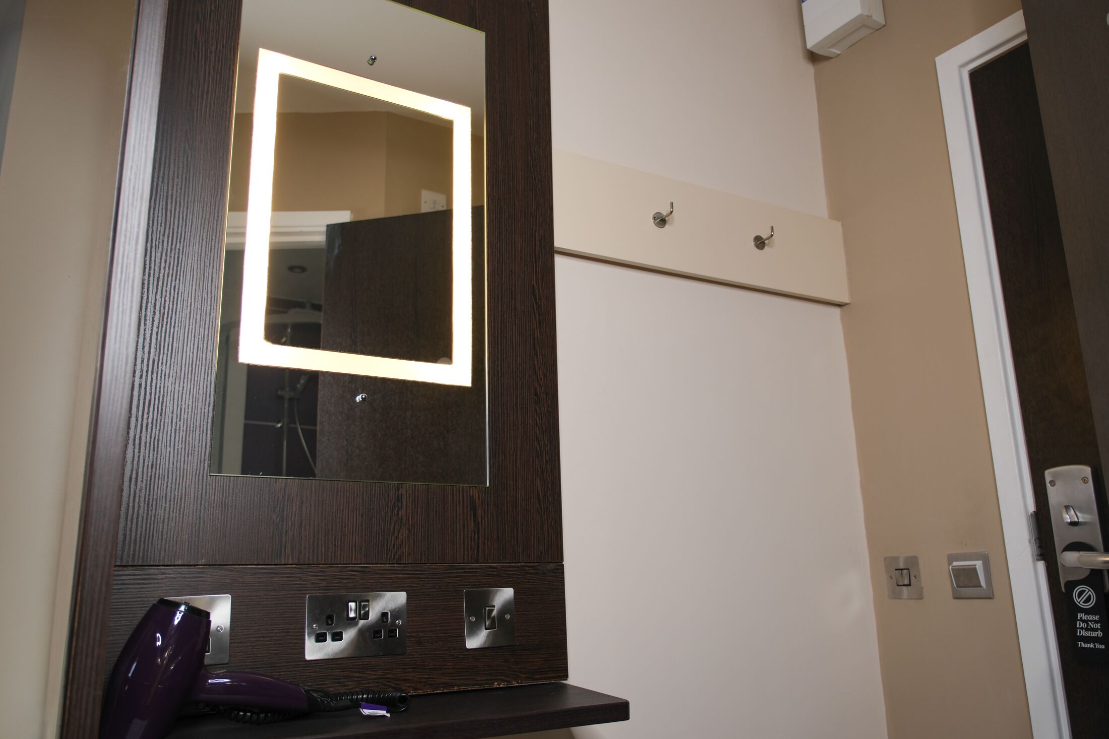 Un bagno con un mobile lavabo in legno, uno specchio con illuminazione e una porta con un cartello.