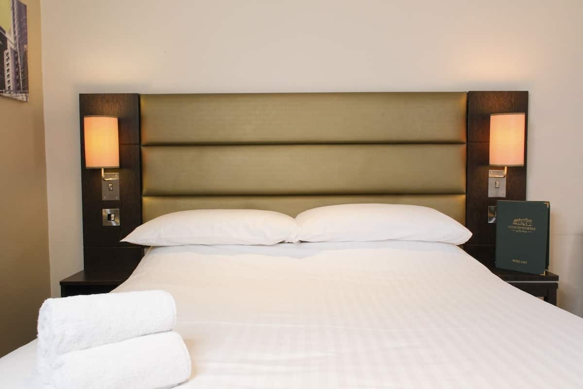 Una cama bien hecha con sábanas blancas, dos almohadas y dos lámparas de noche a cada lado.