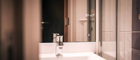 Un baño con lavamanos blanco, cabina de ducha con mampara de vidrio y espejo.