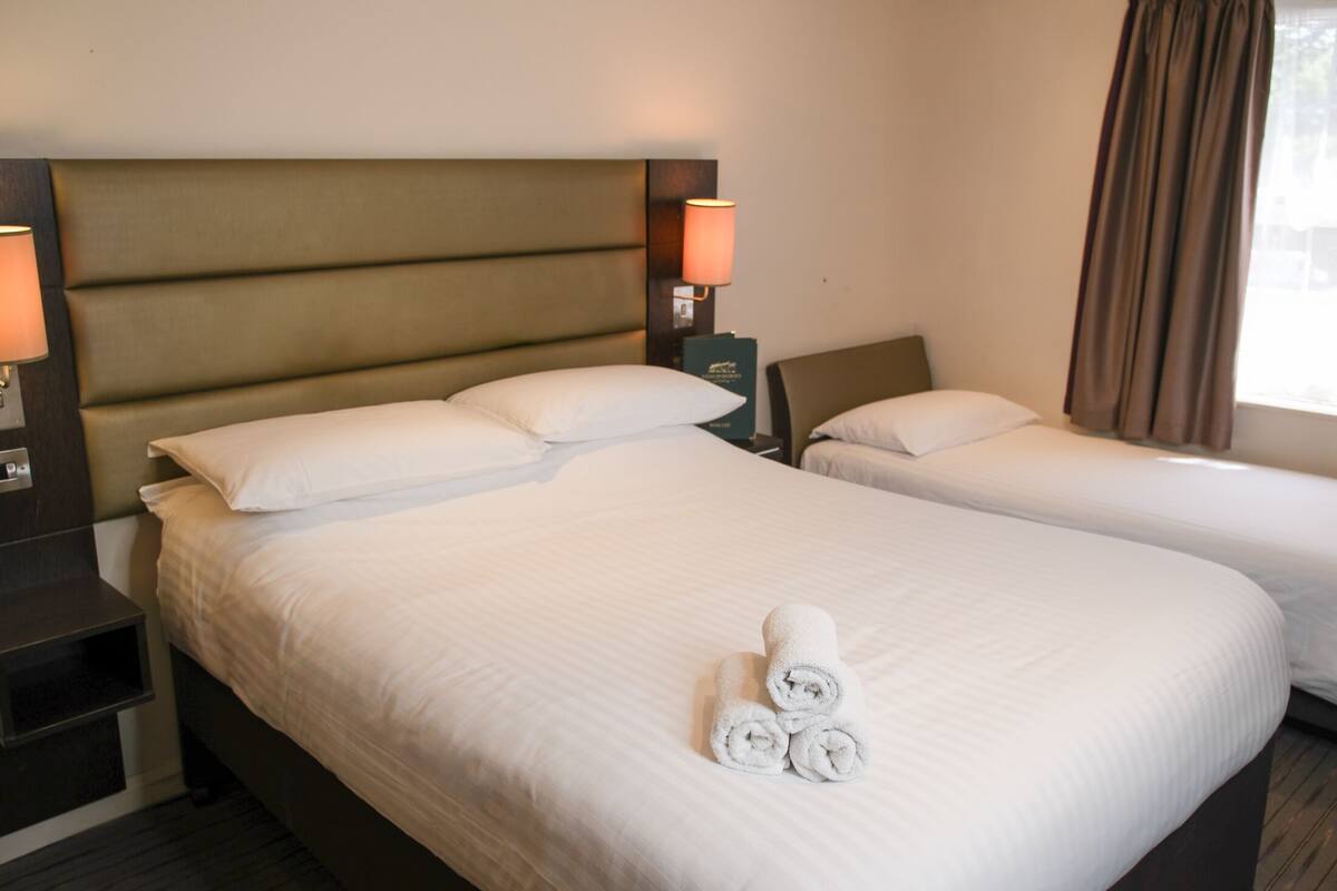 Habitación de hotel con una cama grande, dos mesitas de noche, una lámpara y una ventana con cortinas.